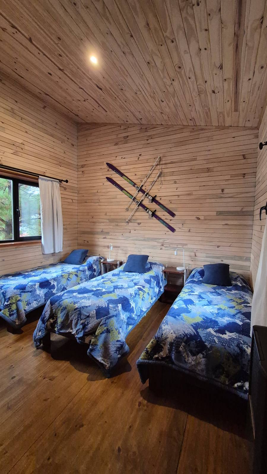 Habitación con tres camas simples y esquís antiguos en la pared