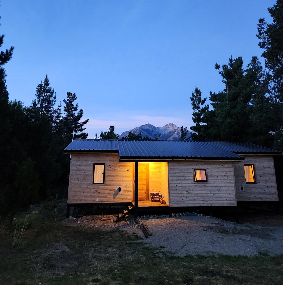 La cabaña de madera iluminada al atardecer, con la montaña detrás
