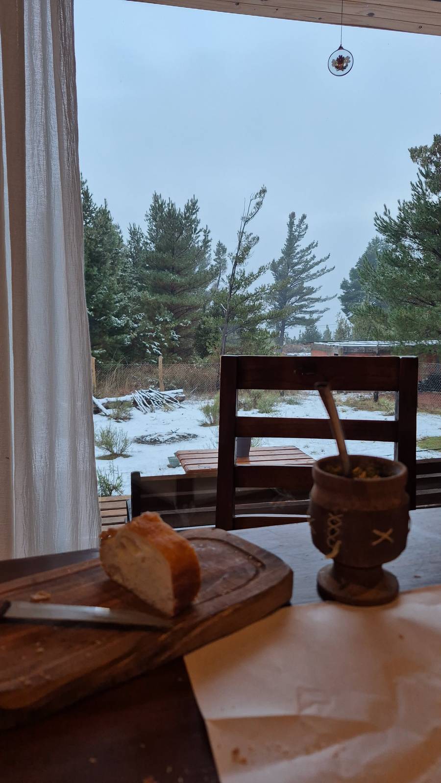 Mate y pan sobre la mesa, con el terreno nevado del otro lado de la ventana
